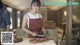 A woman in an apron cutting up a piece of meat on a cutting board.