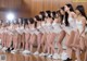 A group of young women in white bodysuits standing on a basketball court.