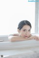 A woman laying in a bathtub with her hand on the edge of it.